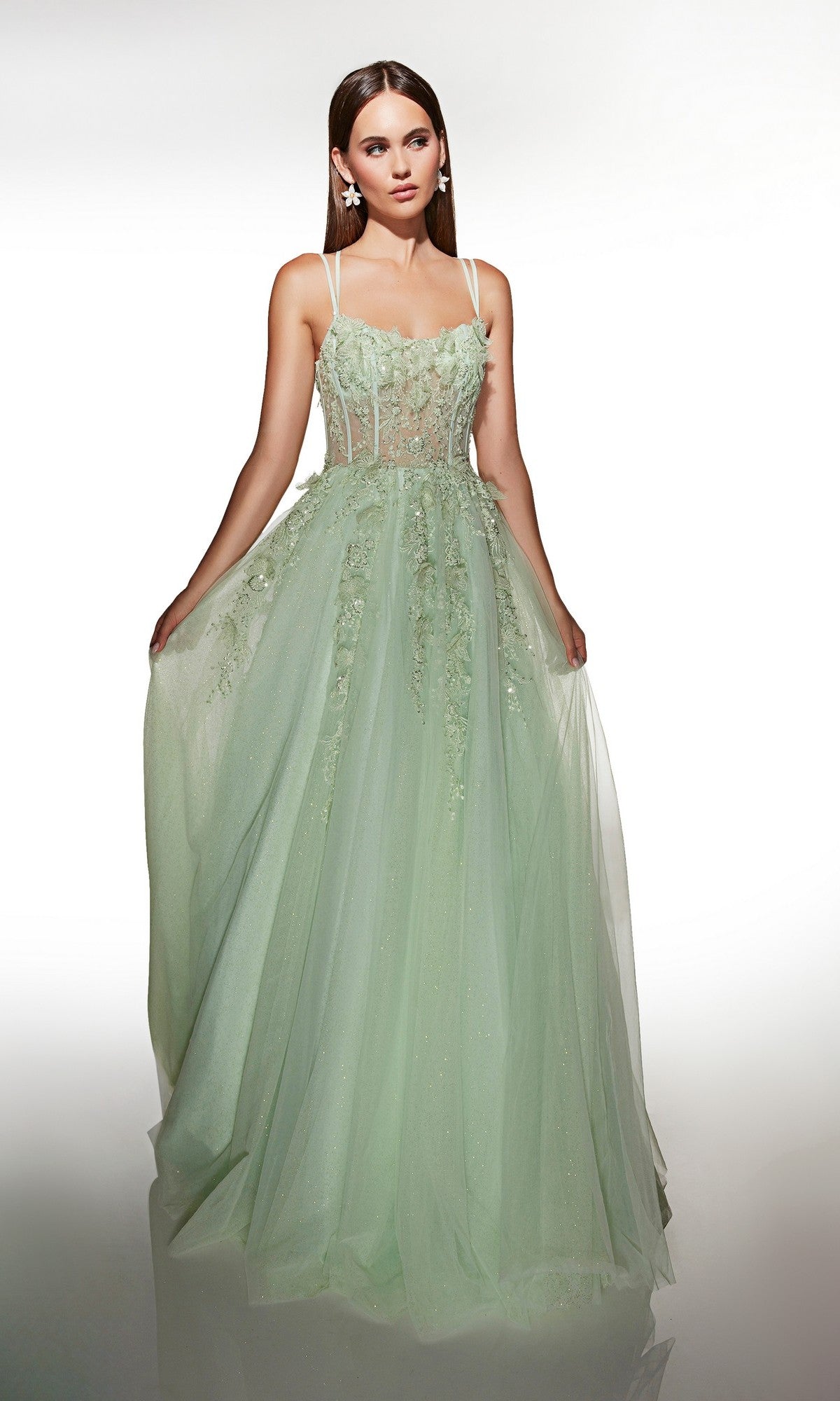 A woman models the Alyce 62203 long prom dress in light green, featuring glitter tulle, 3D floral appliques, and a sheer bodice, standing against a plain white background.